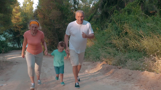 祖母祖父和小孙子手拉手在森林里的道路上奔跑视频