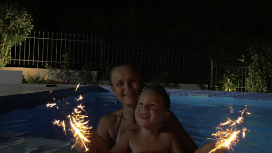 女人和小男孩晚上在游泳池里点烟花视频