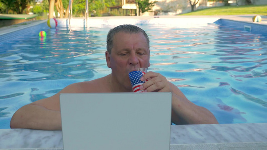 游泳池里的男人边看电脑边喝果汁视频