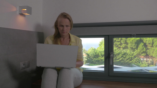 金发女人坐房间里用笔记本电脑上工作视频