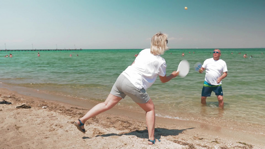 两位老人在阳光明媚的海滩上打羽毛球视频