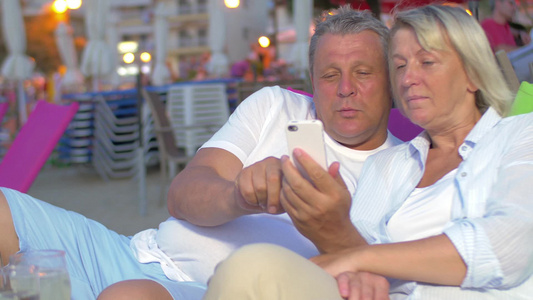 老年人在晚上在海滩上放松时使用手机视频