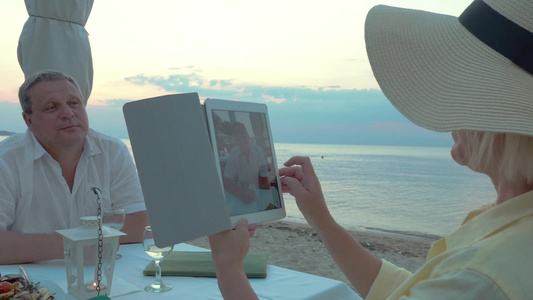 老年夫妇在海滩户外餐厅吃晚饭拍照视频