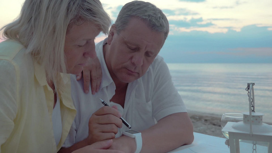 一对老年夫妇在海边的桌子上看智能手表视频