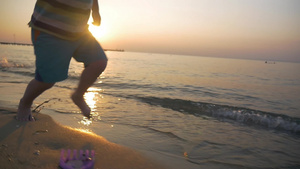 一个赤脚的小男孩在温暖的阳光下沿着潮湿的沙滩里奔跑28秒视频