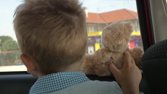 坐车旅行时小男孩与玩具熊看着窗外视频