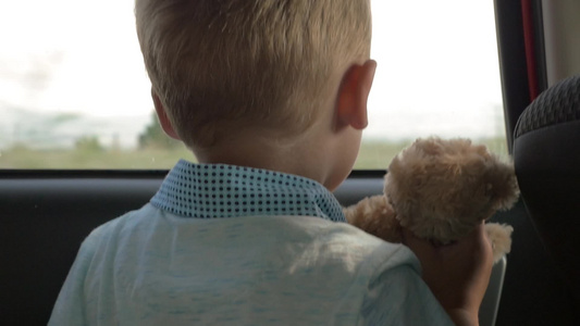 拿着玩具熊的小男孩正在看着窗外风景视频