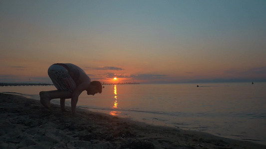 一个年轻人在日落时在海滩上做倒立和双手行走的缓慢动作视频