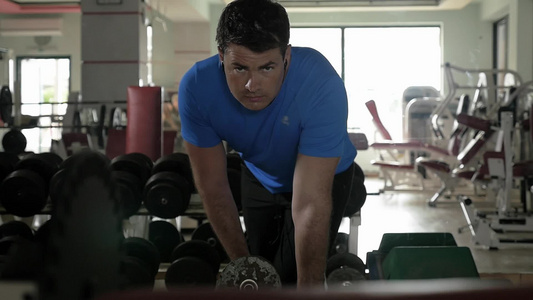 一个强壮的男人在健身房戴着耳机听音乐同时锻炼哑铃视频
