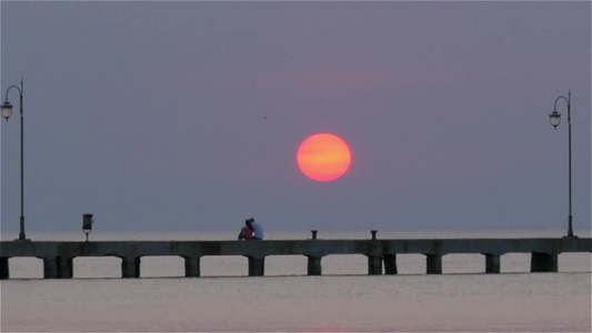 夕阳下的海面码头浮桥情侣依偎而坐视频