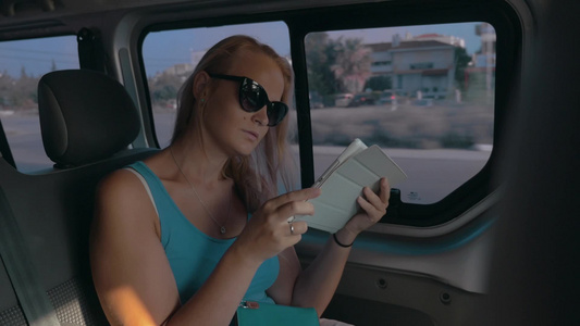 年轻的女人戴着太阳镜坐在行驶的车里用数字平板电脑工作视频