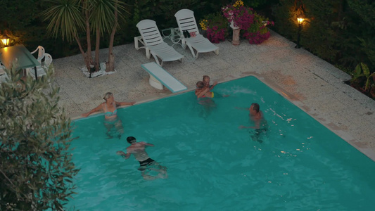 夜晚一家人在室外游泳池快乐地游泳玩耍的高角度镜头视频