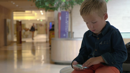 小男孩在购物中心看着智能手机上的照片视频