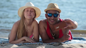 快乐的夫妇躺在海滩上后面是海洋背景上用手机自拍12秒视频