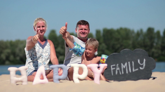 欢快的家庭坐在海滩上竖起大拇指前景有快乐的英文字母视频