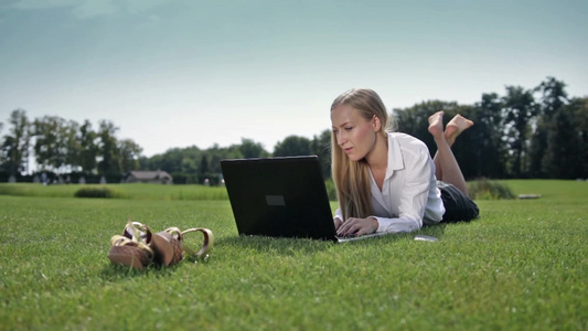 年轻女性躺在绿草地上操作笔记本电脑[二十多岁]视频