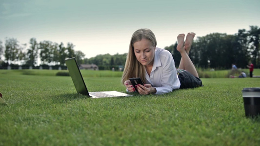 商务女性赤脚躺在草坪操作手机电脑视频