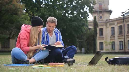 一对学生坐在草地上读一本书视频