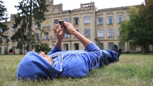 男学生躺在草地上浏览手机视频