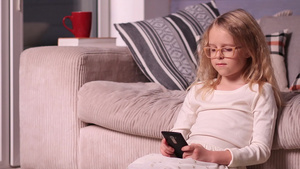 可爱的小女孩坐在沙发附近的地板上玩手机14秒视频