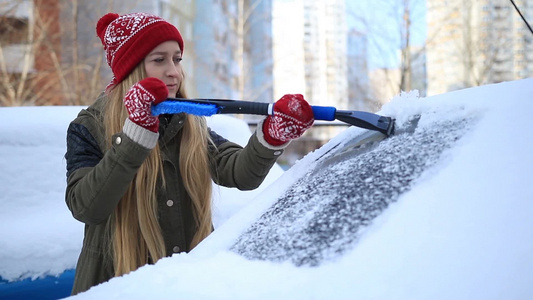 年轻女性铲除汽车挡风玻璃上冰和雪视频