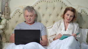 坐在床上看书和玩电脑的夫妇20秒视频