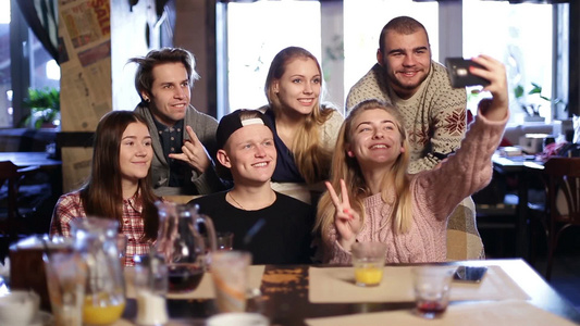 一群年轻人在咖啡馆里用智能手机自拍[品牌手机]视频