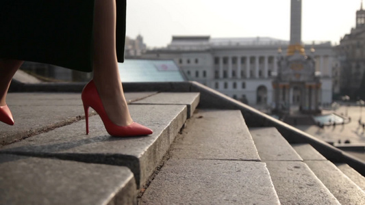 穿着绿色大衣和橙色高跟鞋的女性优雅地走在城市的石头楼梯上视频