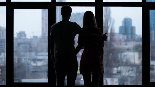  一对深情的夫妇站在宽阔的窗户旁互相拥抱视频