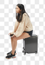年轻女孩坐在行李箱上玩平板电脑图片