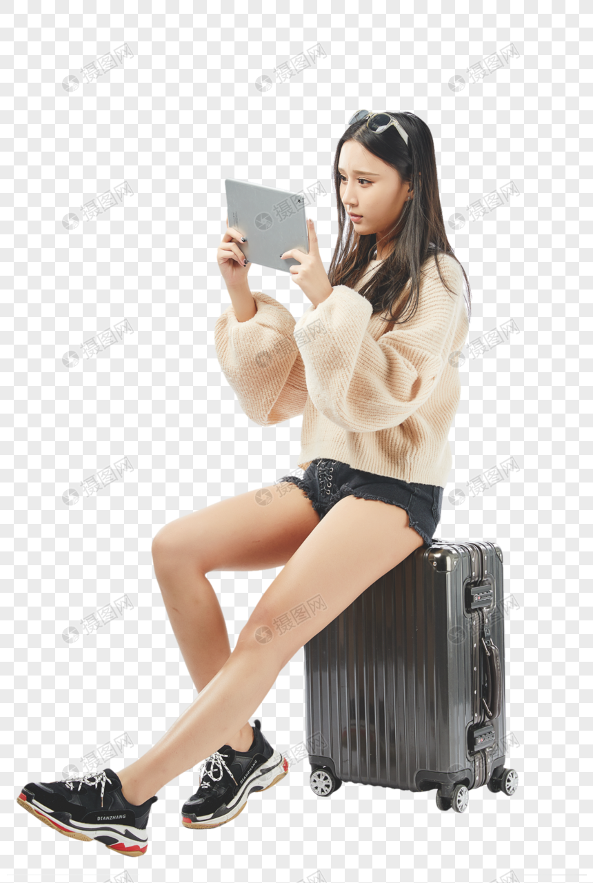 年轻女孩坐在行李箱上玩平板电脑图片