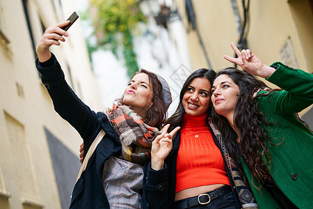 多种族的三个快乐的女人城市背景下用智能手机拍张自拍照片三个快乐的女人户外起散步图片