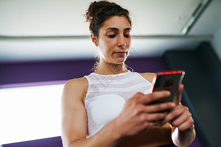 运动女性健身房用她的智能手机咨询她的训练女人智能手机上咨询她的培训图片