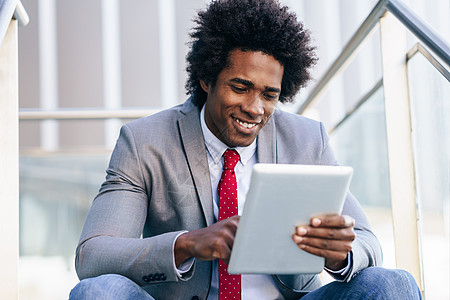 坐办公楼附近用数字平板电脑的黑人商人有AFRO头发的男人坐办公楼附近用数字平板电脑的黑人商人图片