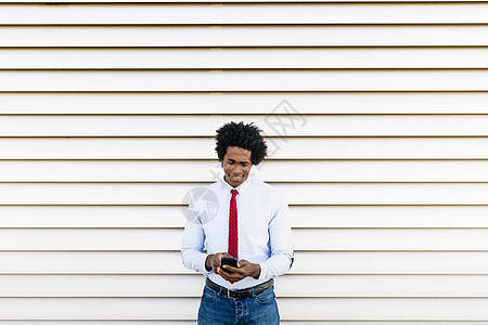 黑色商人用智能手机在白色百叶窗背景前图片