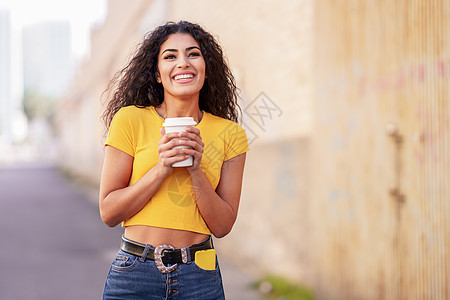 年轻的阿拉伯女人带着外卖咖啡穿过城市街道阿拉伯女孩带着外卖咖啡走街面图片