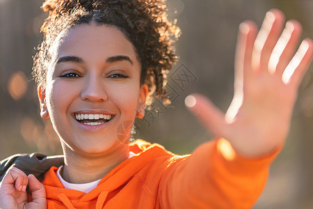 户外肖像美丽的快乐混合种族非裔美国女孩十几岁的女性年轻女子笑,挥手微笑与完美的牙齿金色的傍晚阳光图片