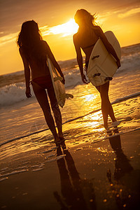 日落或日出的海滩上,两位美丽性感的年轻女性穿着比基尼冲浪的女孩海滩上用白色的冲浪板日落或日出的海滩上冲浪图片