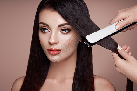理发师用发烫把深色长发伸直长着直发的漂亮女人光滑的发型图片