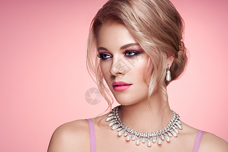 用珠宝描绘美丽的金发女人优雅的发型美容时尚配饰完美的化妆粉红色的背景背景图片