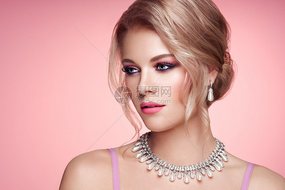 用珠宝描绘美丽的金发女人优雅的发型美容时尚配饰完美的化妆粉红色的背景图片