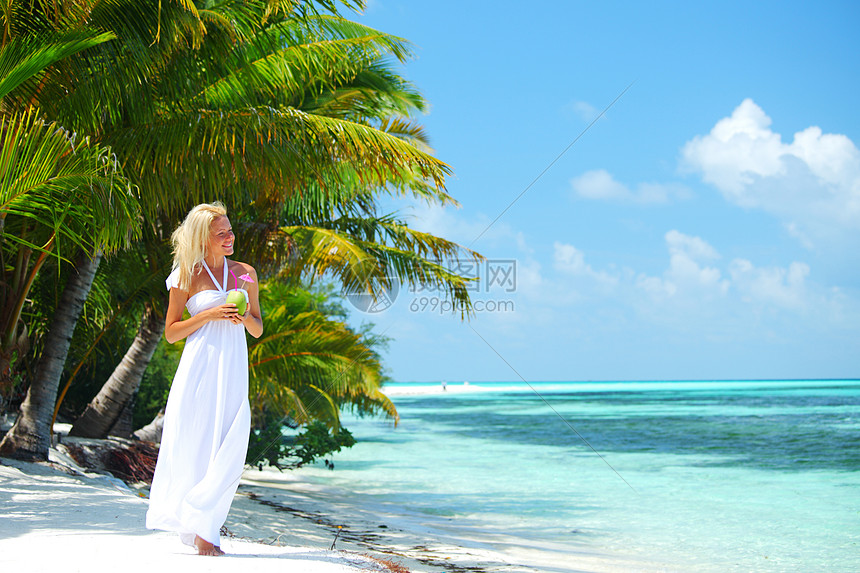 穿着白色长裙的女人热带海滩上散步,棕榈树着椰子鸡尾酒,微笑着海滩上有椰子鸡尾酒的女人图片
