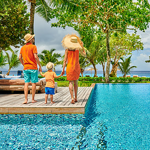 家人靠池边,年轻的夫妇三岁的蹒跚学步的男孩塞舌尔马赫的度假游泳池图片