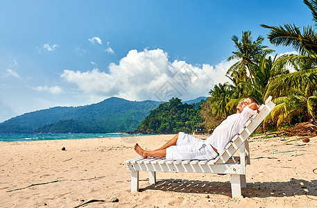 马来西亚提曼岛的热带海滩上,穿着白色衣服的男人太阳床上放松图片