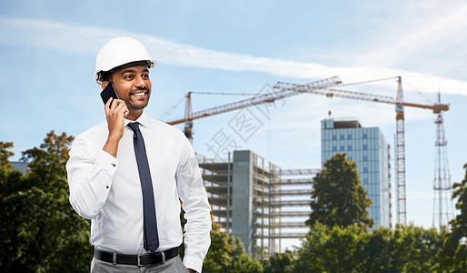 建筑,建筑业务人的微笑的印度男建筑师头盔调用智能手机建筑现场背景建筑师建筑工地打电话给智能手机图片