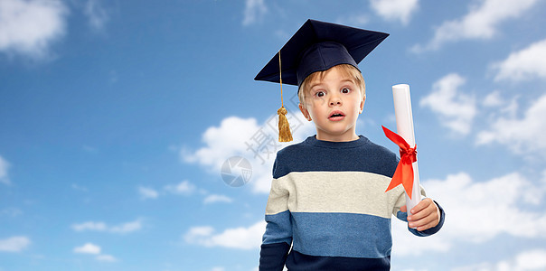 学校,教育学的惊讶的小男孩戴着学士帽或灰泥板,文凭蓝天背景灰泥板上的小男孩,天空上有文凭图片