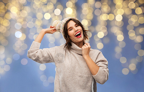 圣诞节,假日庆祝快乐的微笑年轻女子针织冬帽毛衣节日灯上的蓝色背景圣诞节戴冬帽毛衣的年轻女人图片