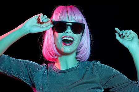 风格,时尚夜生活的快乐的年轻女人戴着粉红色的假发黑色霓虹灯的黑暗背景穿着粉红色假发黑色太阳镜的快乐女人图片