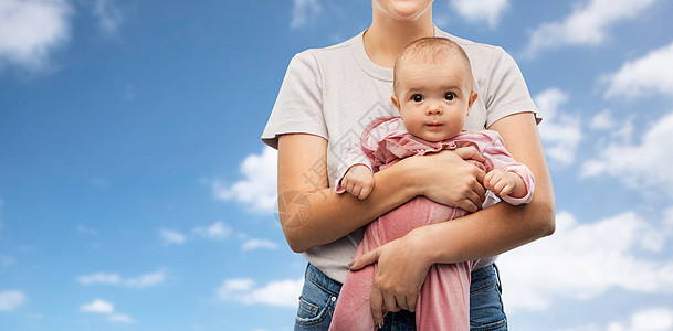 家庭,孩子父母的快乐的微笑年轻母亲抱着小宝贝女儿蓝天云彩的背景快乐的年轻母亲抱着小女儿图片