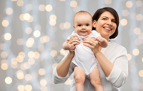 家庭,孩子父母的快乐的微笑中年母亲抱着小宝贝女儿节日的灯光背景快乐的中年母亲带着孩子灯光下图片